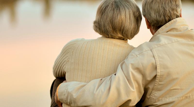 old couple holding each other in front of lake